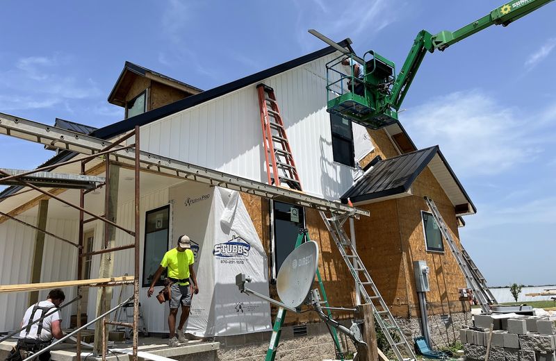 Crew working from a lift to side a two-story addition