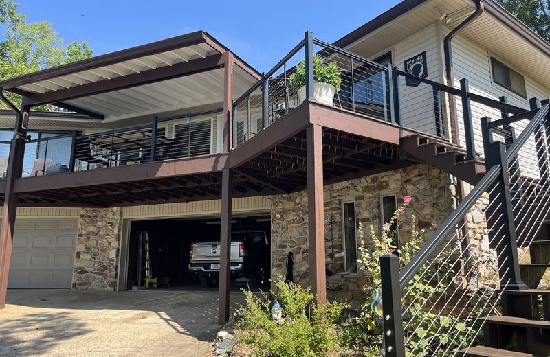 A covered deck with cable railing built above a stone-faced garage